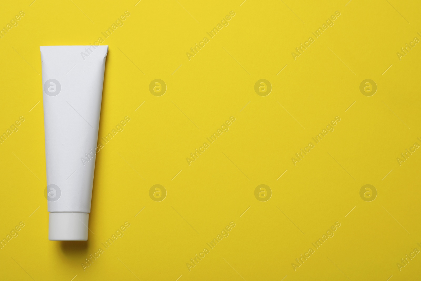 Photo of Blank tube of toothpaste on yellow background, top view. Space for text