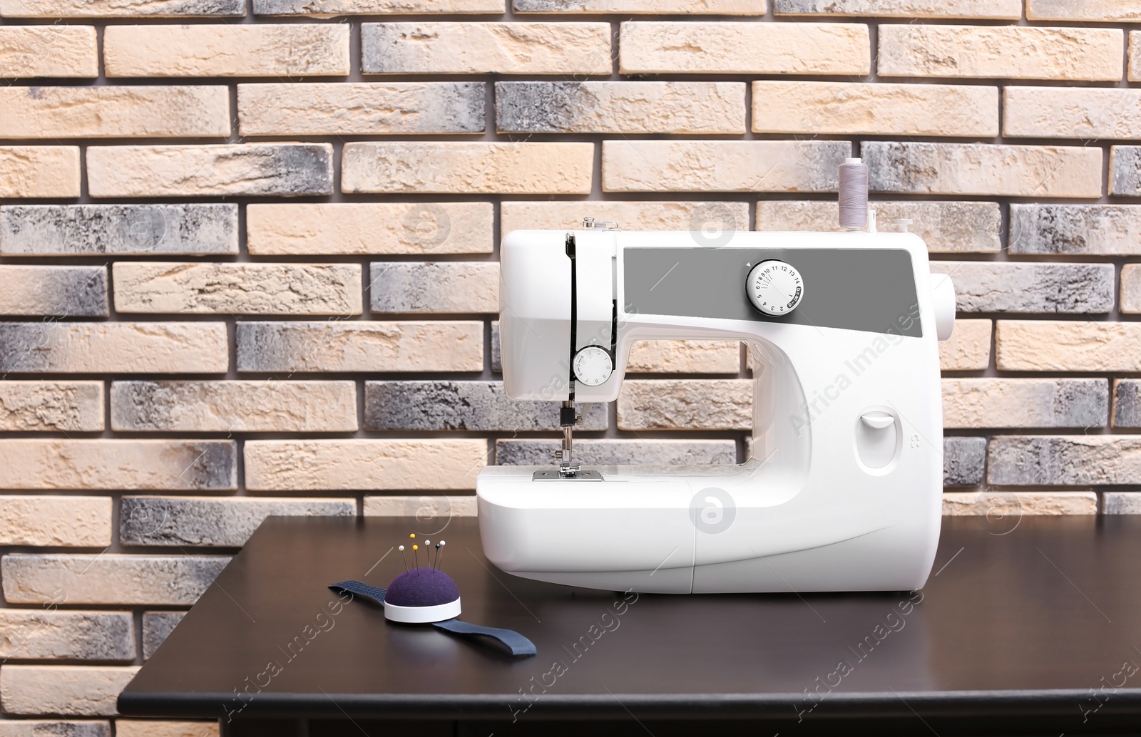 Photo of Modern sewing machine on table near brick wall