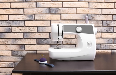 Photo of Modern sewing machine on table near brick wall