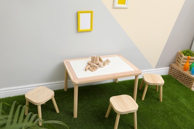 Stylish playroom interior with table, stools and green carpet