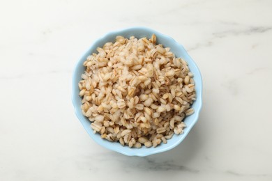 Photo of Delicious pearl barley in bowl on white marble table, top view