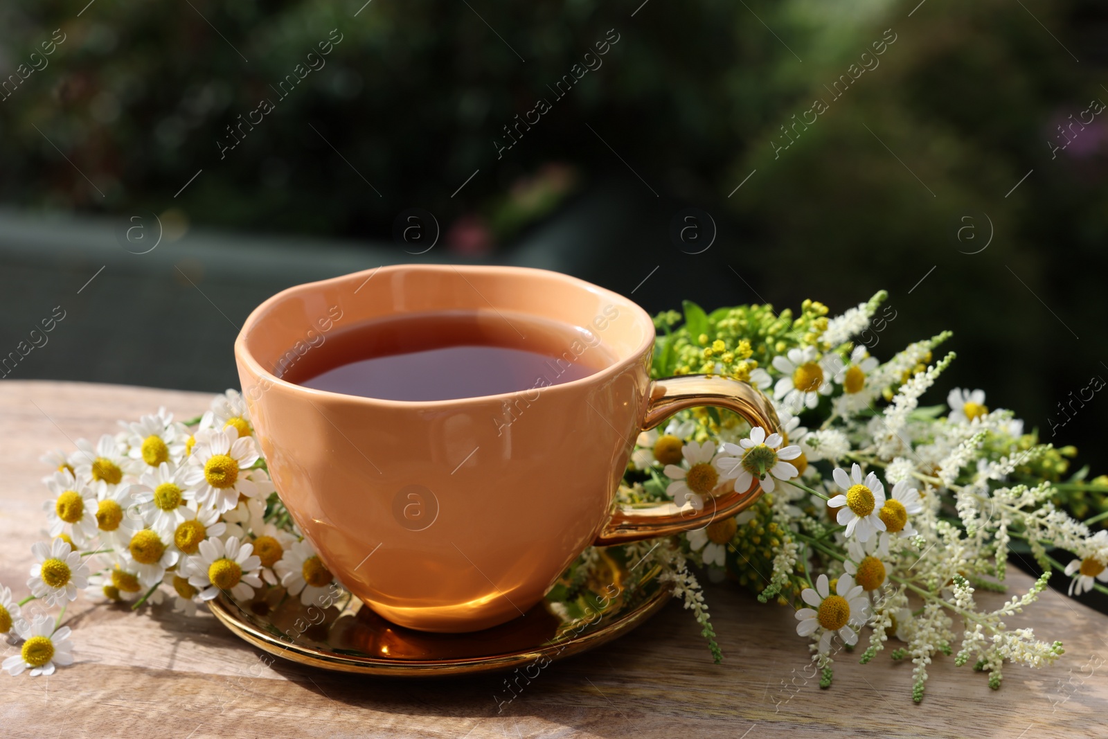 Photo of Cup of delicious chamomile tea and fresh flowers outdoors on sunny day