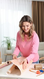 Beautiful young woman wrapping gift at table in living room