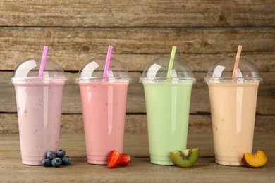 Photo of Plastic cups with different tasty smoothies and fresh fruits on wooden table