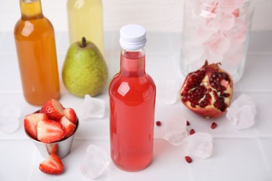 Photo of Tasty kombucha in glass bottles, fresh fruits and ice on white tiled table