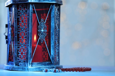 Photo of Arabic lantern and misbaha on table against blurred lights, space for text