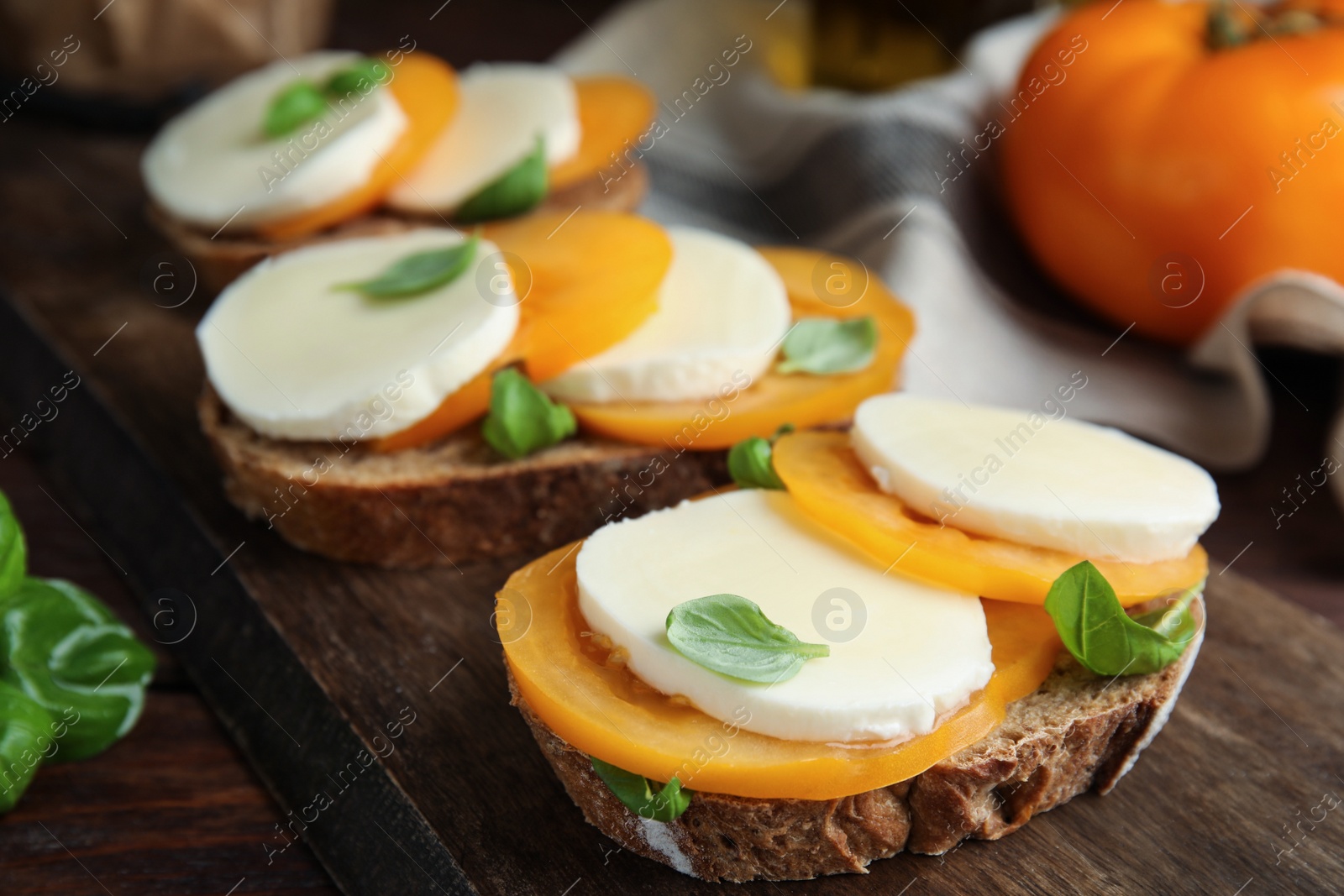 Photo of Delicious sandwiches with mozzarella, yellow tomatoes and basil on wooden board