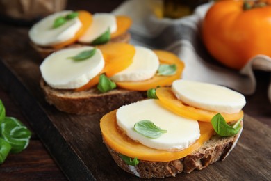 Photo of Delicious sandwiches with mozzarella, yellow tomatoes and basil on wooden board