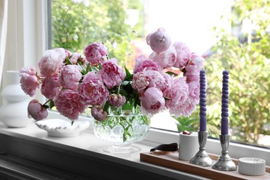 Beautiful pink peonies in vase and tray with candles on window sill. Interior design