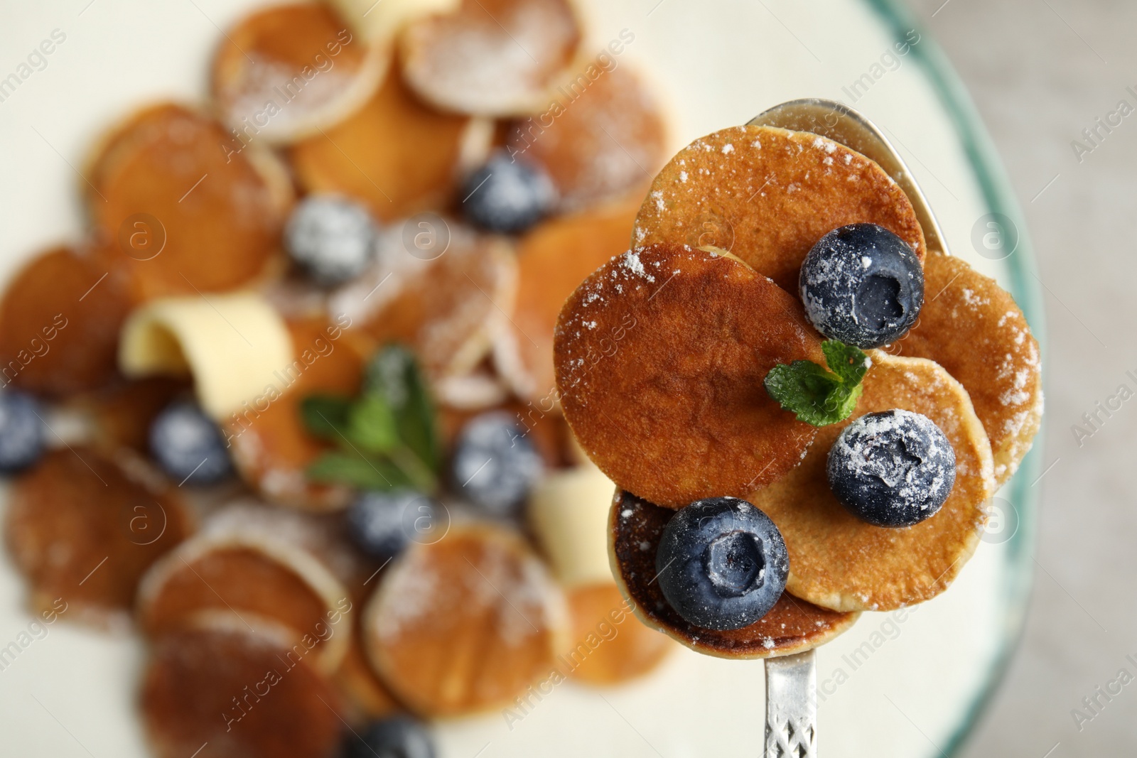 Photo of Spoon with cereal pancakes, blueberries and mint on blurred background, closeup. Space for text