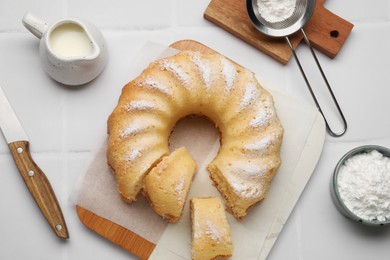 Photo of Delicious sponge cake served on white tiled table, flat lay