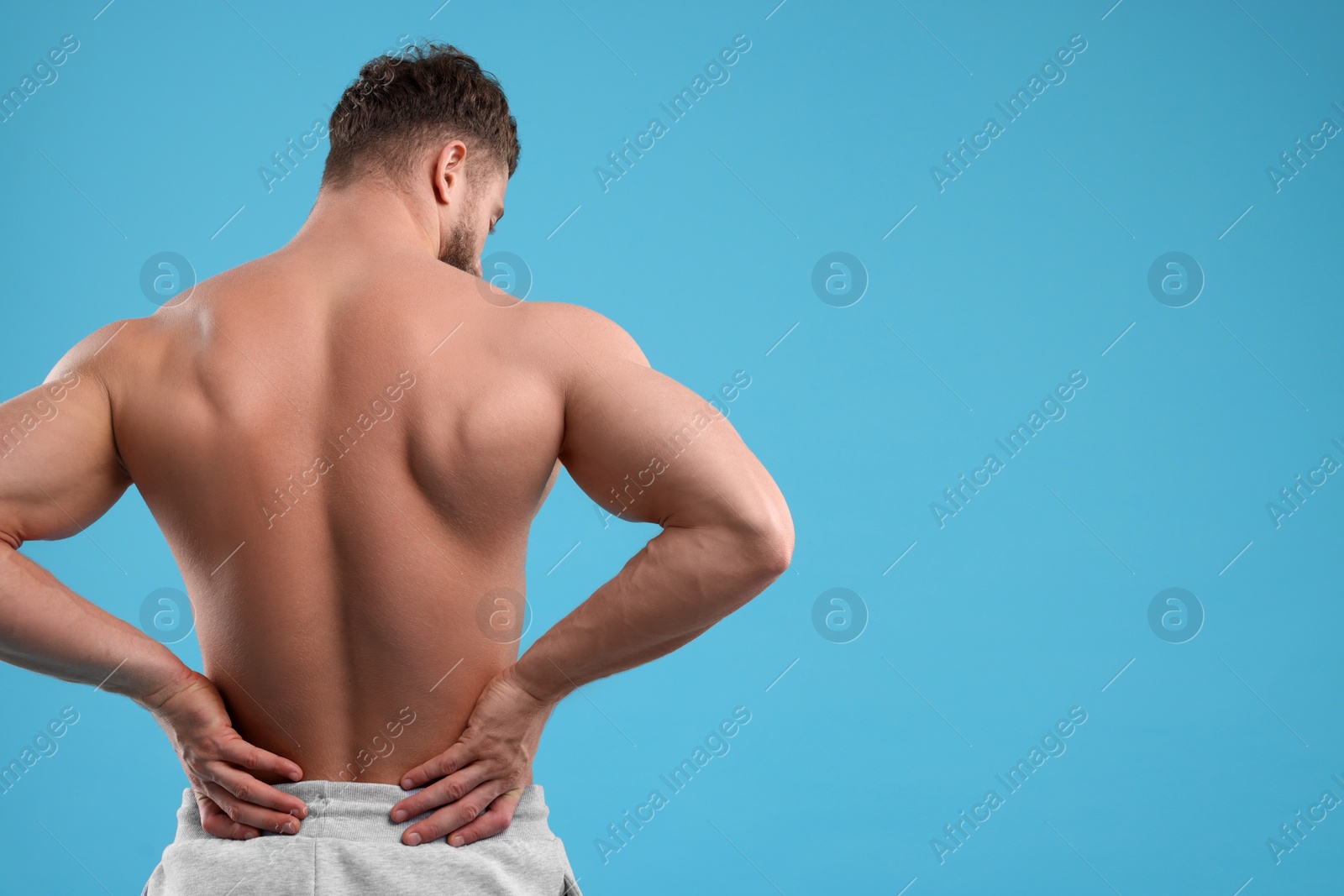Photo of Man suffering from back pain on light blue background, back view. Space for text