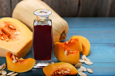 Fresh pumpkin seed oil in glass bottle on blue wooden table. Space for text