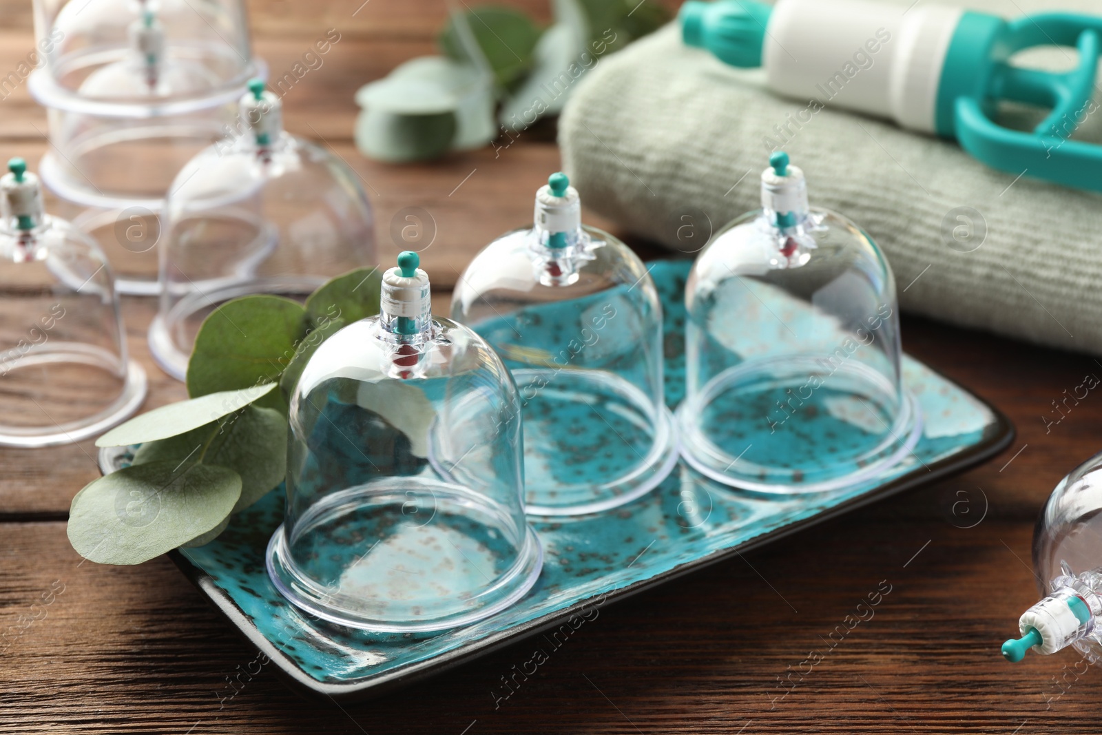 Photo of Plastic cups and eucalyptus leaves on wooden table. Cupping therapy