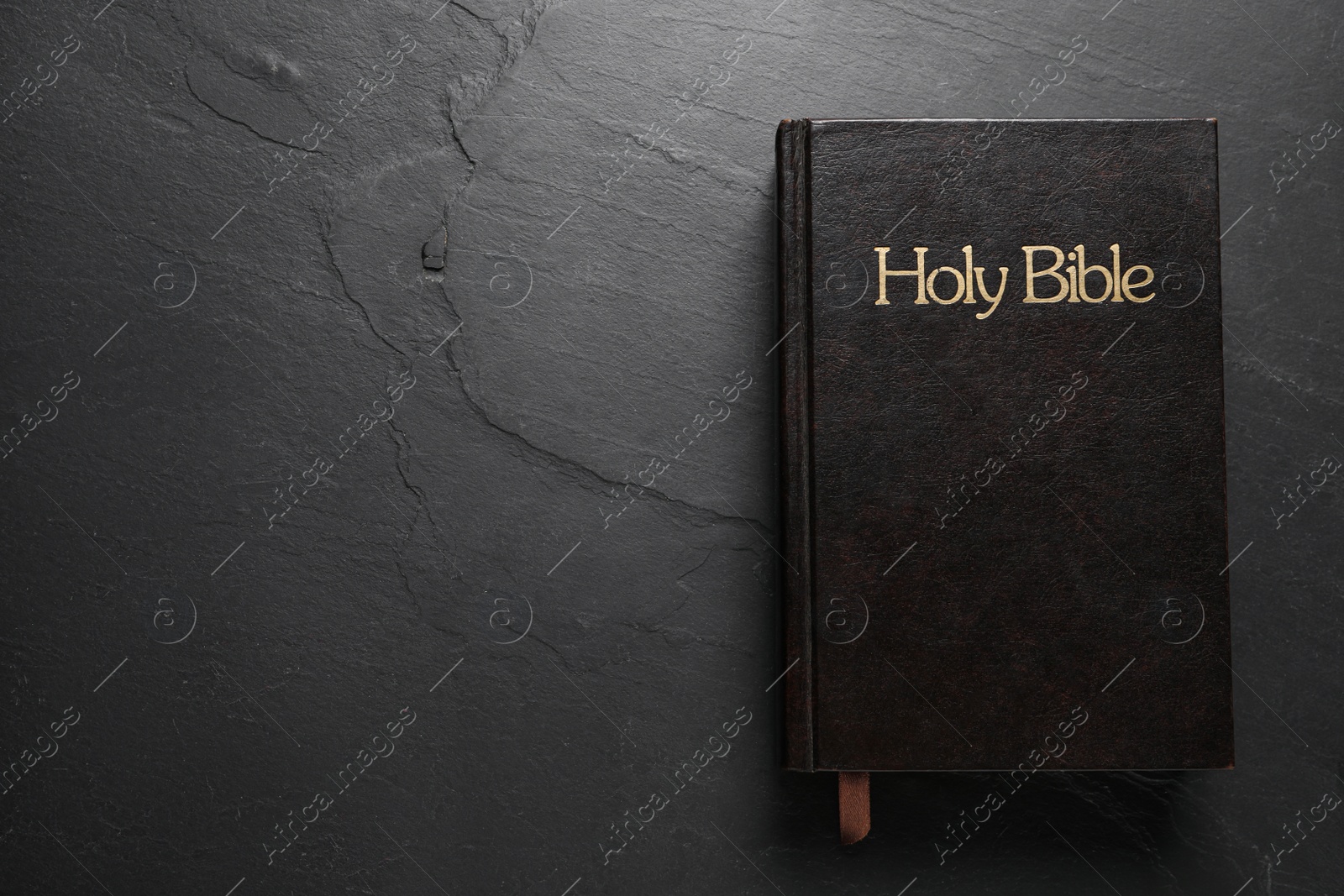 Photo of Hardcover Bible on black table, top view with space for text. Religious book
