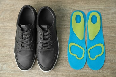 Photo of Orthopedic insoles near shoes on floor, flat lay