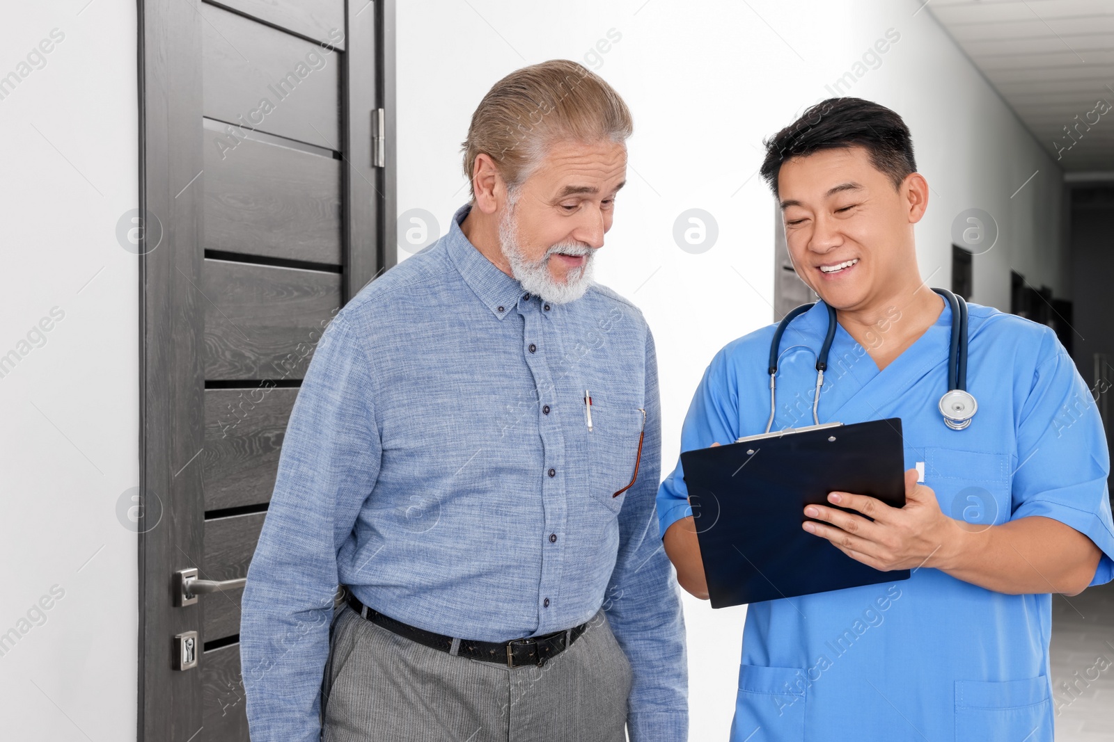 Photo of Doctor with clipboard consulting senior patient in clinic