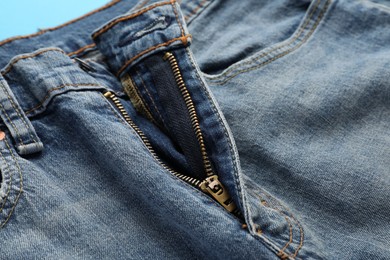 Photo of Jeans with unbuttoned fly on light blue background, closeup. Exhibitionist concept