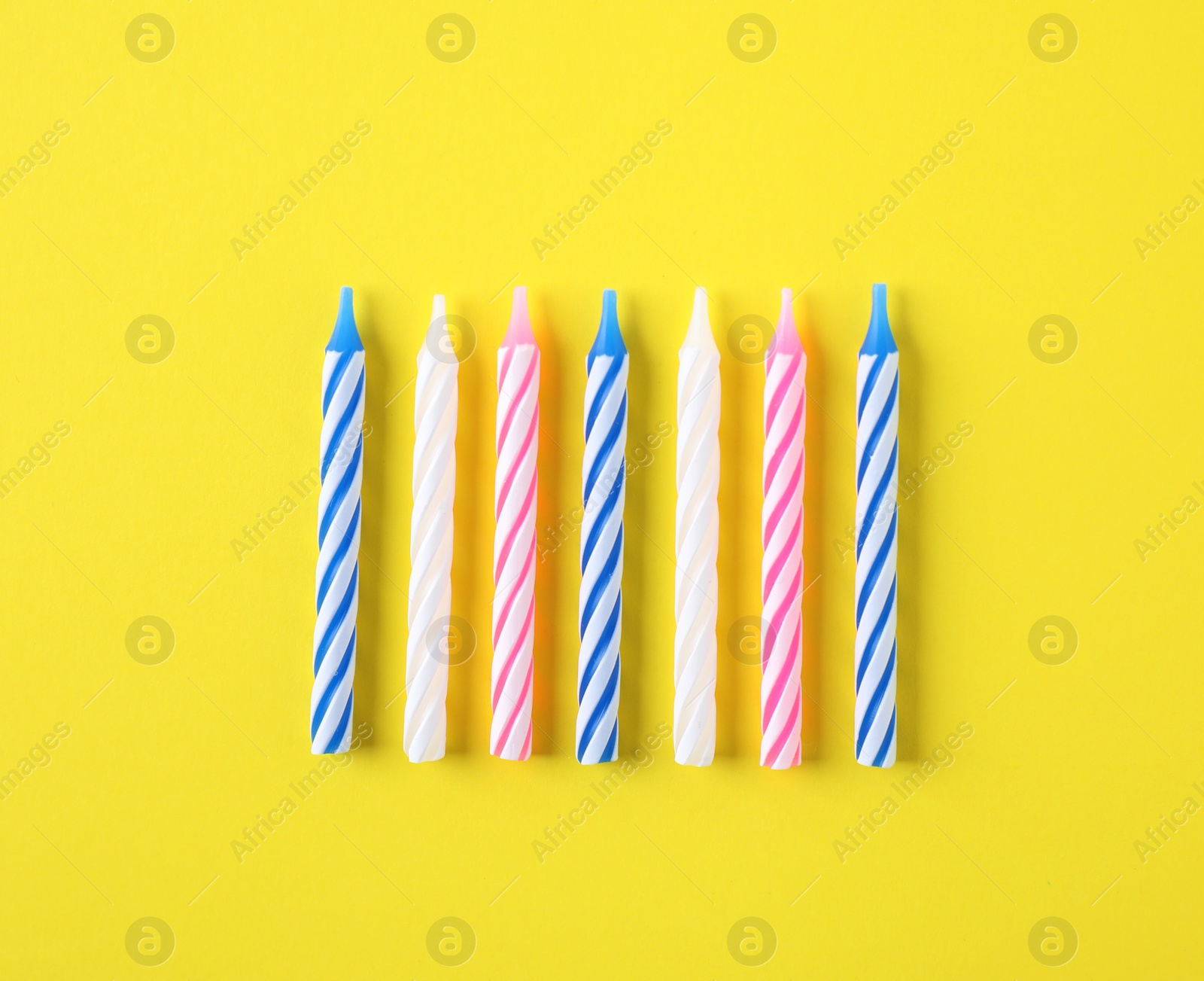 Photo of Colorful striped birthday candles on yellow background, flat lay