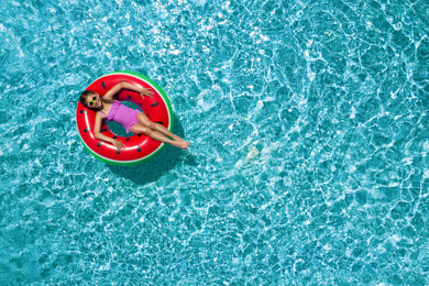 Cute little girl with inflatable ring in swimming pool, top view. Space for text