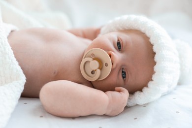 Cute newborn baby in white knitted hat lying on bed, closeup