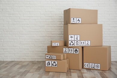 Cardboard boxes with different packaging symbols on floor near white brick wall, space for text. Parcel delivery