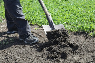Photo of Gardener digging soil with shovel in garden, closeup