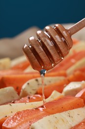 Pouring honey onto slices of parsnip and carrot against blue background, closeup