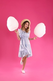 Happy young woman with cotton candies on pink background