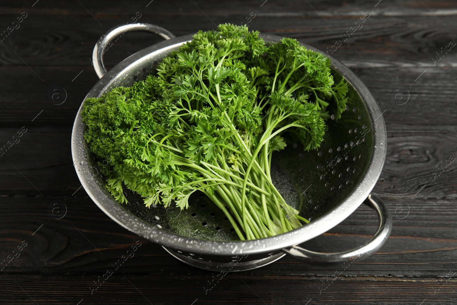 Photo of Colander with fresh green parsley on dark wooden table