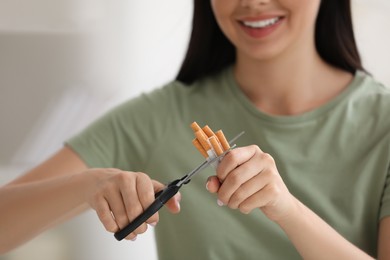Photo of Stop smoking concept. Woman cutting cigarettes on light background, closeup