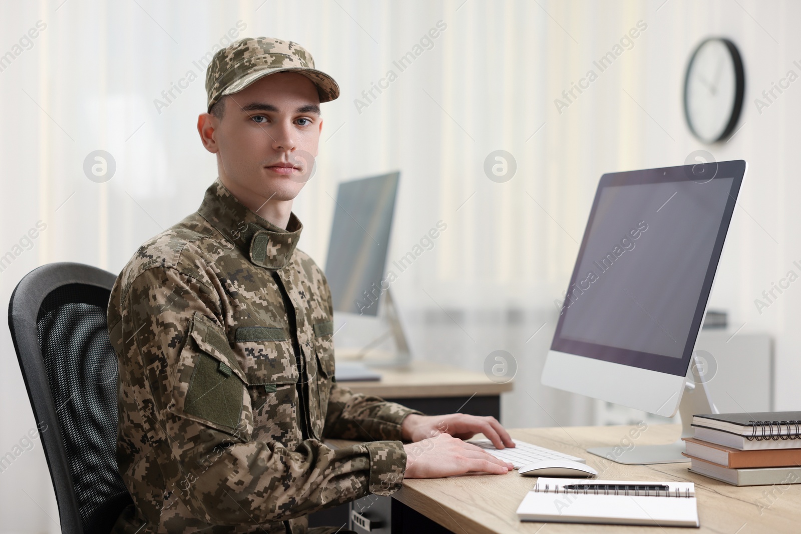 Photo of Military service. Young soldier working with computer at wooden table in office