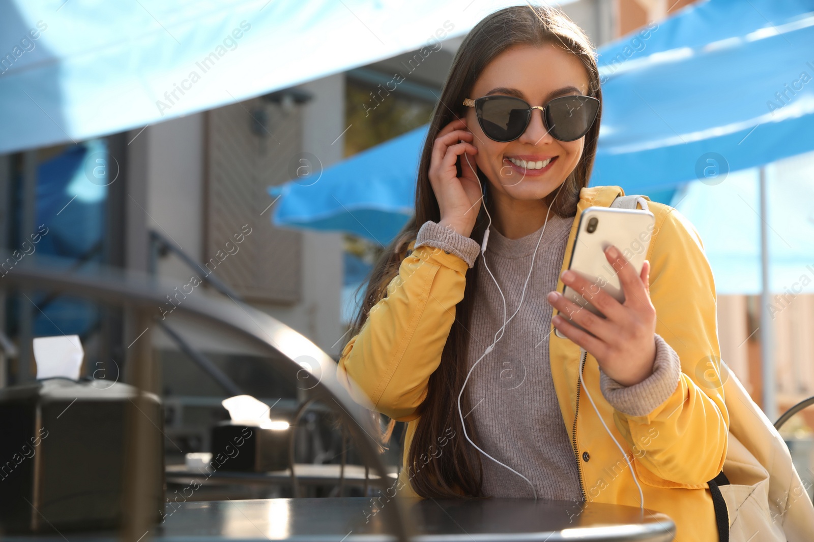 Photo of Happy young woman with earphones and mobile phone listening to music in outdoor cafe