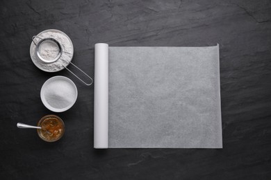 Photo of Roll of baking parchment paper and ingredients on black slate background, flat lay