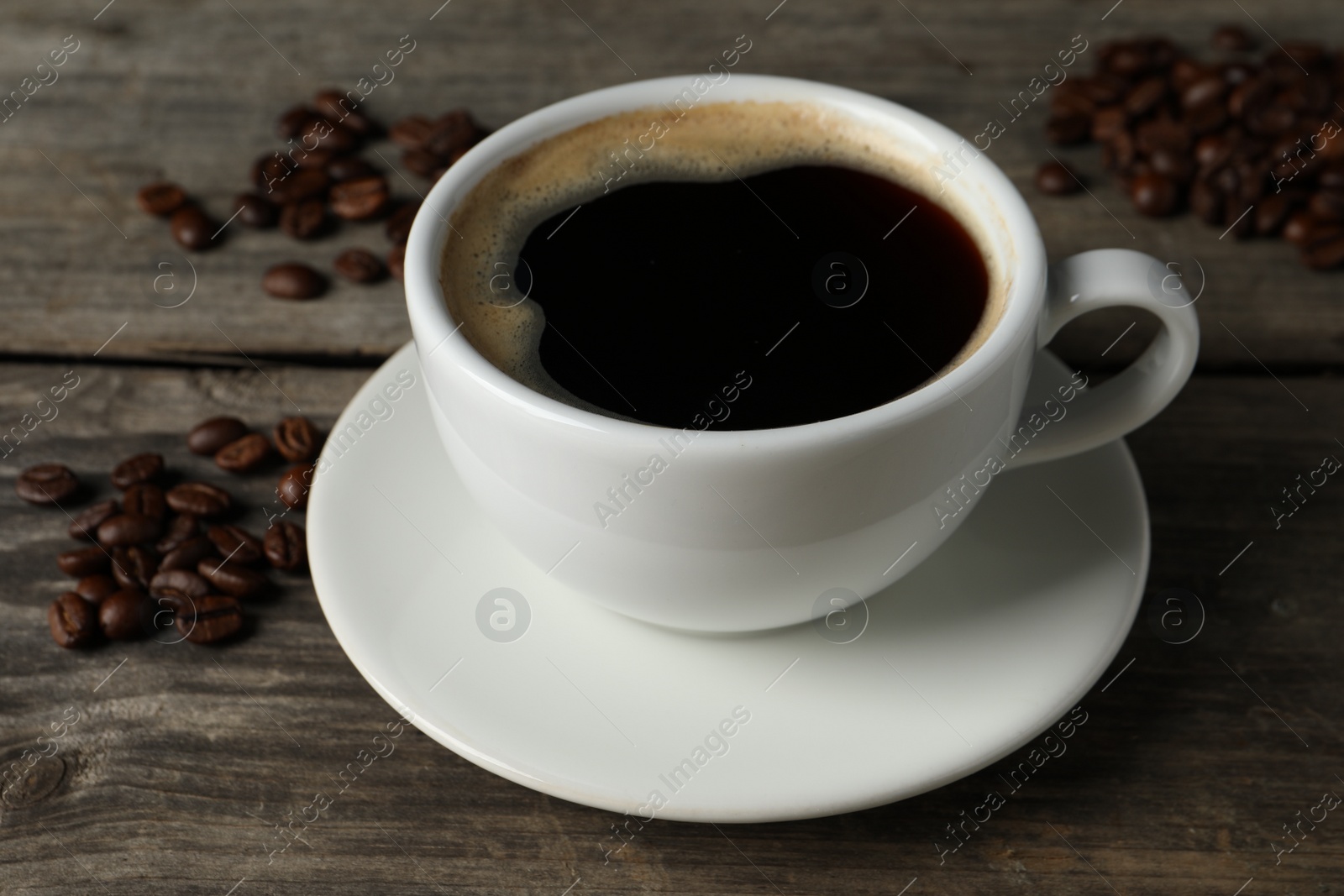 Photo of Cup of hot aromatic coffee and roasted beans on wooden table