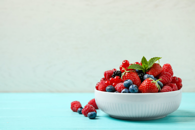 Photo of Mix of different fresh berries and mint in bowl on light blue wooden table. Space for text