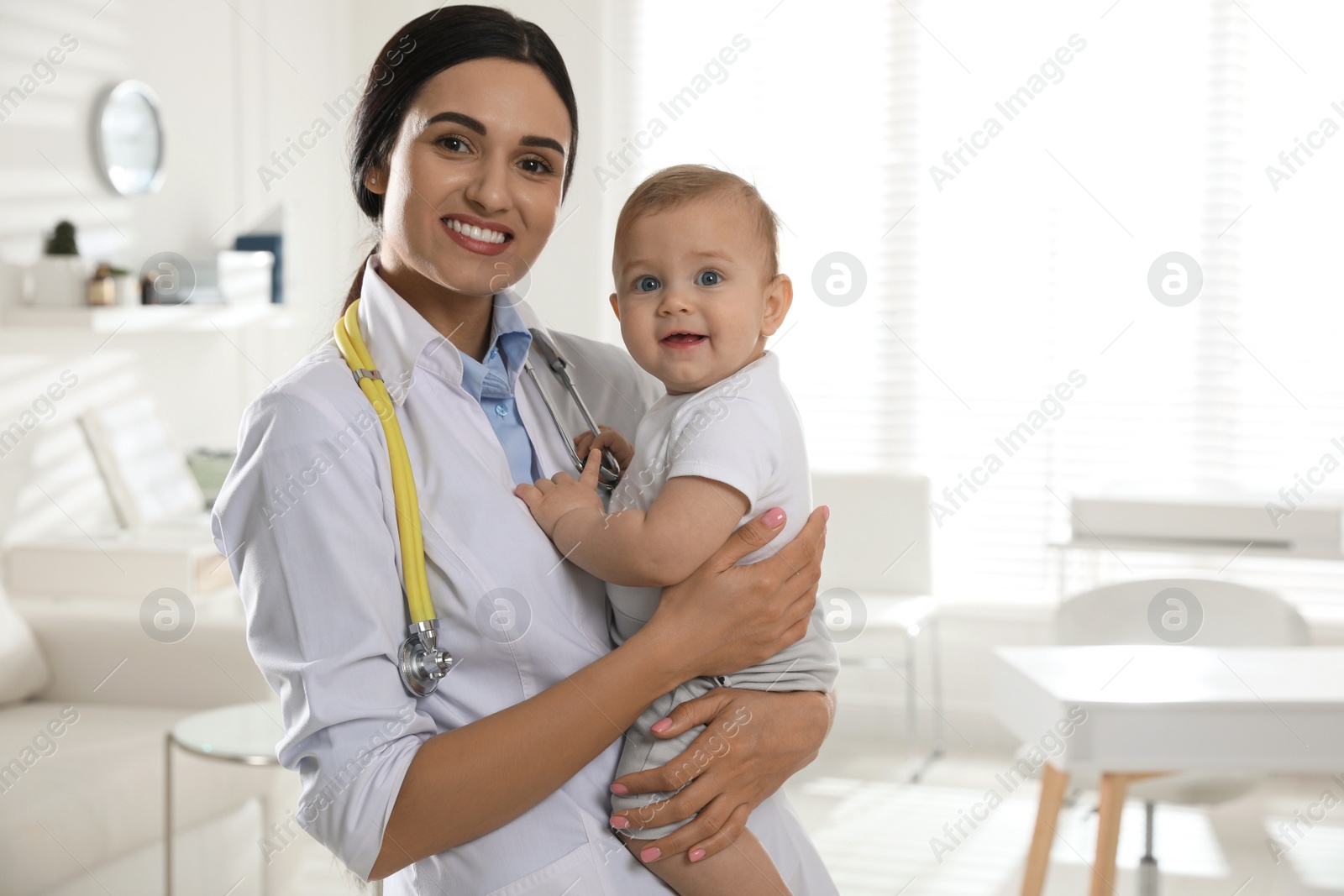 Photo of Young pediatrician with cute little baby in clinic. Space for text