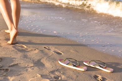 Photo of Closeup of woman and flip flops on sand near sea, space for text. Beach accessories