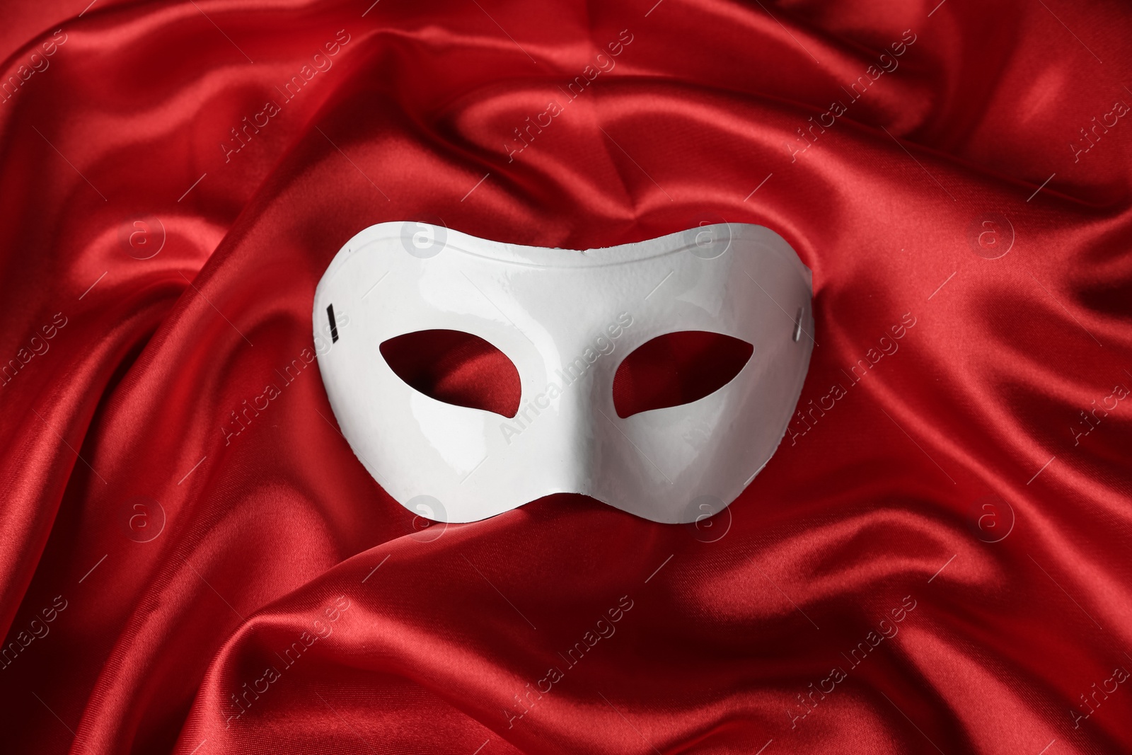 Photo of White theatre mask on red fabric, top view