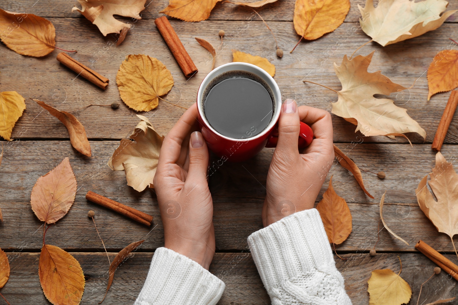 Photo of Woman with cup of hot drink at wooden table, top view. Cozy autumn atmosphere