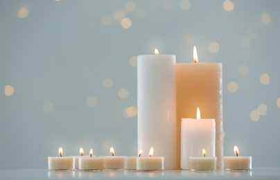 Many burning candles on table against blurred background with bokeh effect