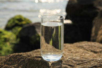 Photo of Glass of fresh water on stone near sea