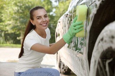 Happy woman washing car with sponge outdoors