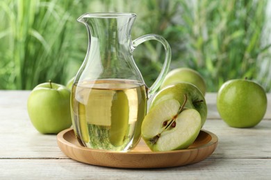 Jug of tasty juice and fresh ripe green apples on white wooden table outdoors