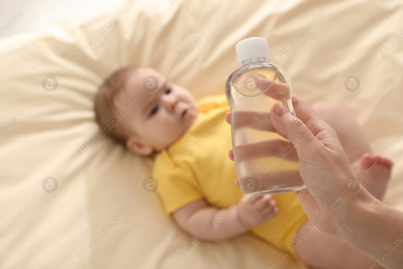 Photo of Mother with bottle of massage oil near baby on bed, closeup