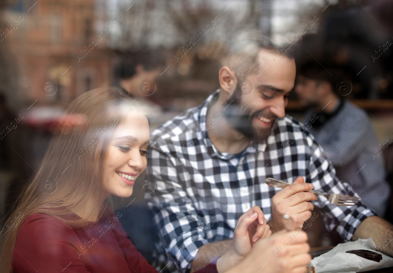 Photo of Lovely young couple spending time together in cafe, view from outdoors through window