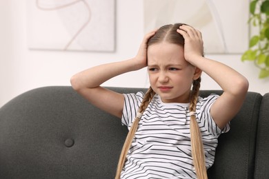 Photo of Little girl suffering from headache on sofa indoors