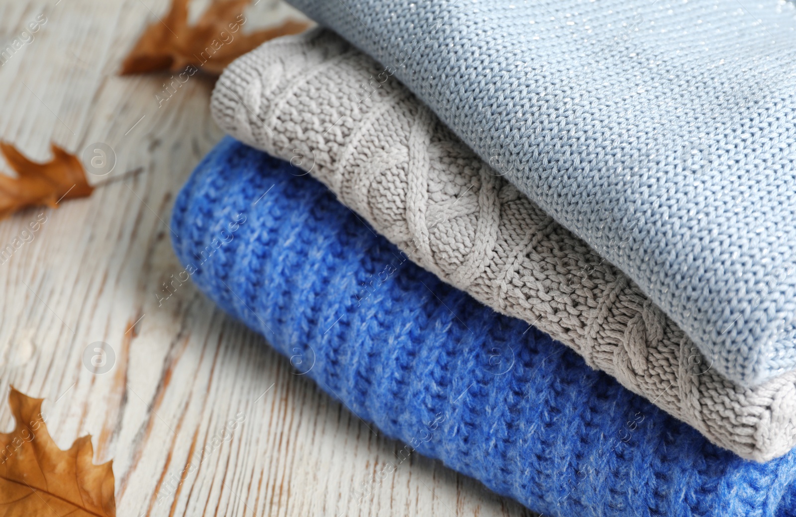 Photo of Stack of folded knitted sweaters and autumn leaves on table, closeup