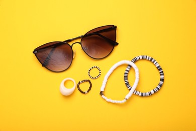 Photo of Stylish sunglasses, bracelets and rings on yellow background, flat lay