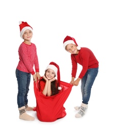 Cute little children in Santa hats with red Christmas bag on white background